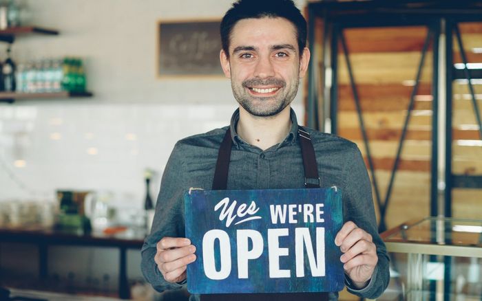 A barista holding an open sign in a cafe