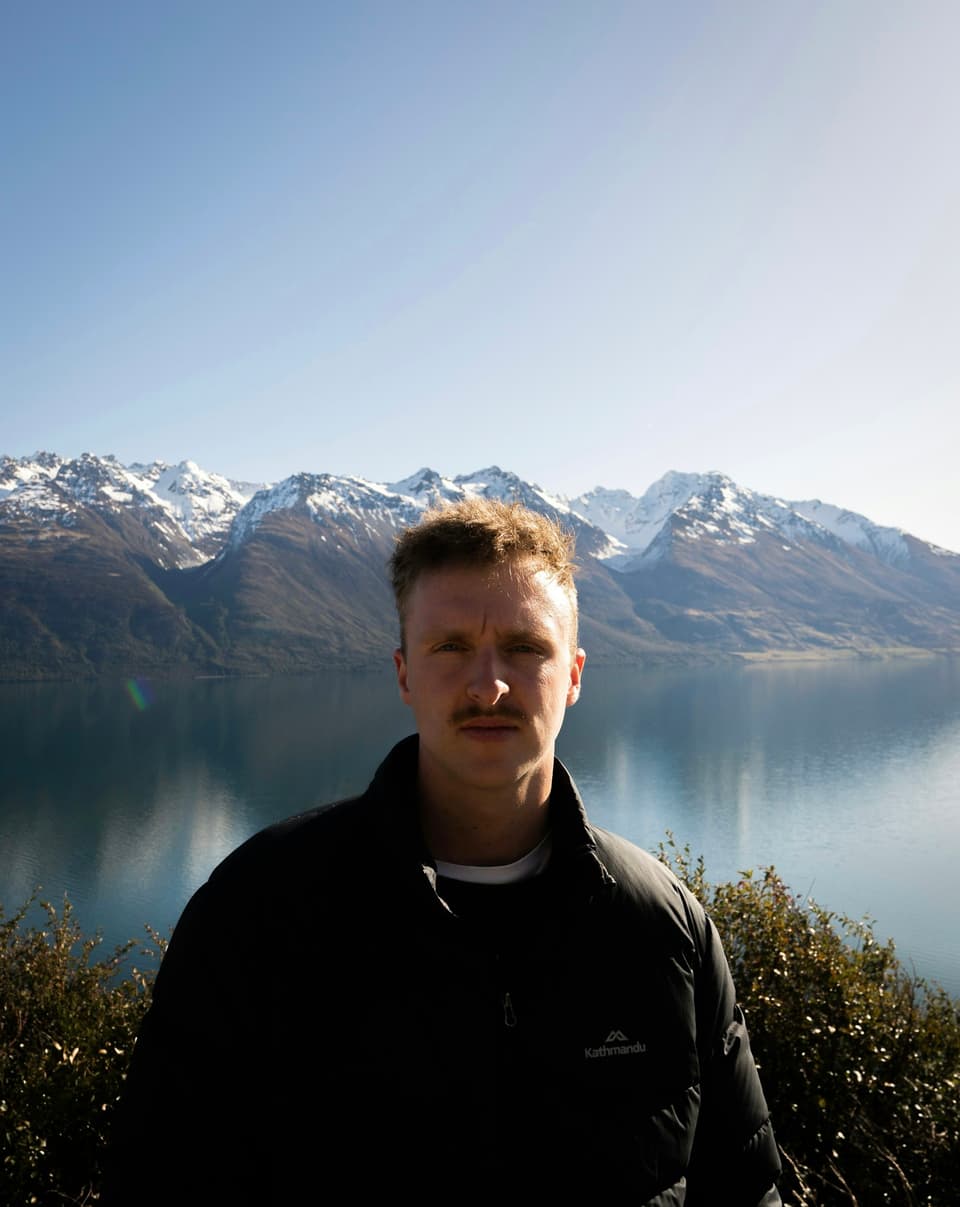 A man standing in front of a New Zealand lake and mountains