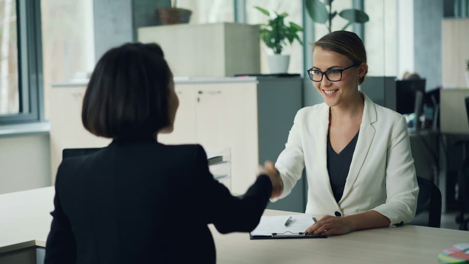 Two business owners shaking hands across a desk