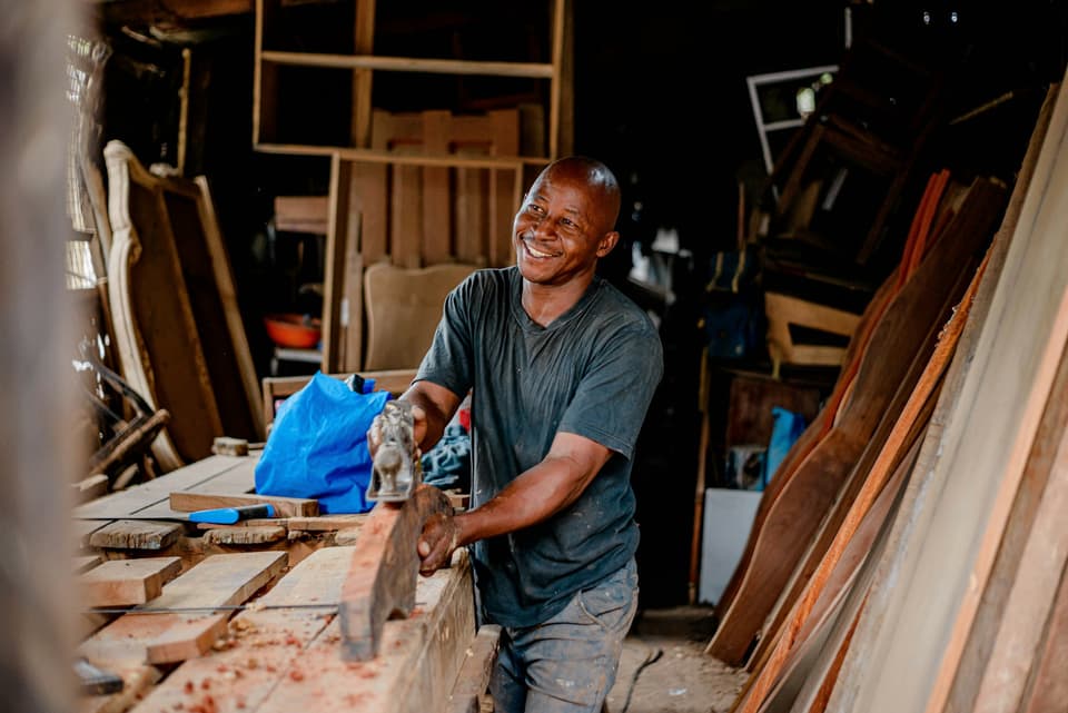 A joiner smiling as he works on a piece of timber in his workshop